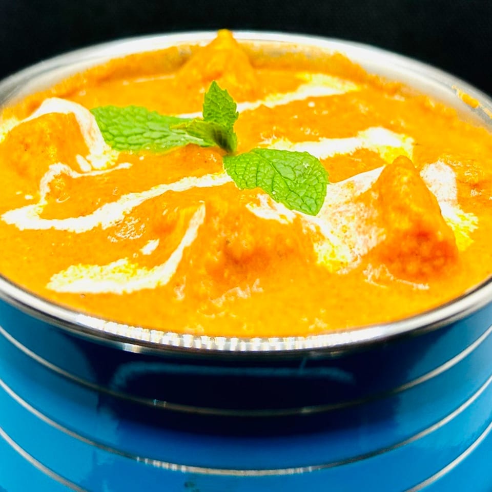 Himalayan Spice Indian Cuisine's creamy orange curry, garnished with fresh mint, in a blue bowl.