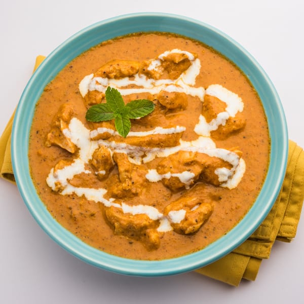 Himalayan Spice Indian Cuisine's butter chicken, garnished with cream and mint, in a blue bowl.