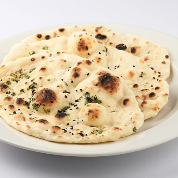 Freshly baked naan bread, garnished with black sesame seeds and herbs, on a white plate.