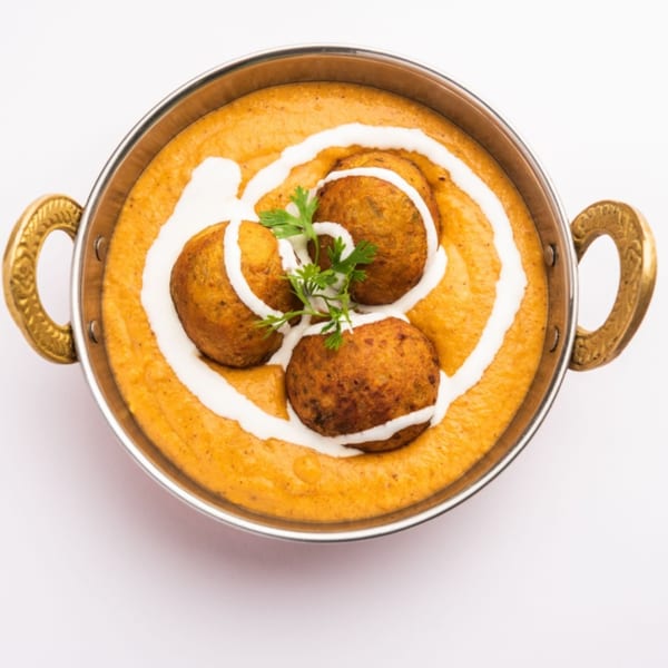 Himalayan Spice Indian Cuisine's Malai Kofta, with three kofta balls in a creamy orange sauce, garnished with cilantro.