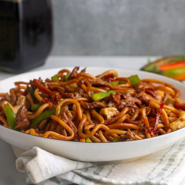 Close-up of a white bowl filled with Himalayan Spice Indian Cuisine's noodles, meat, and vegetables.