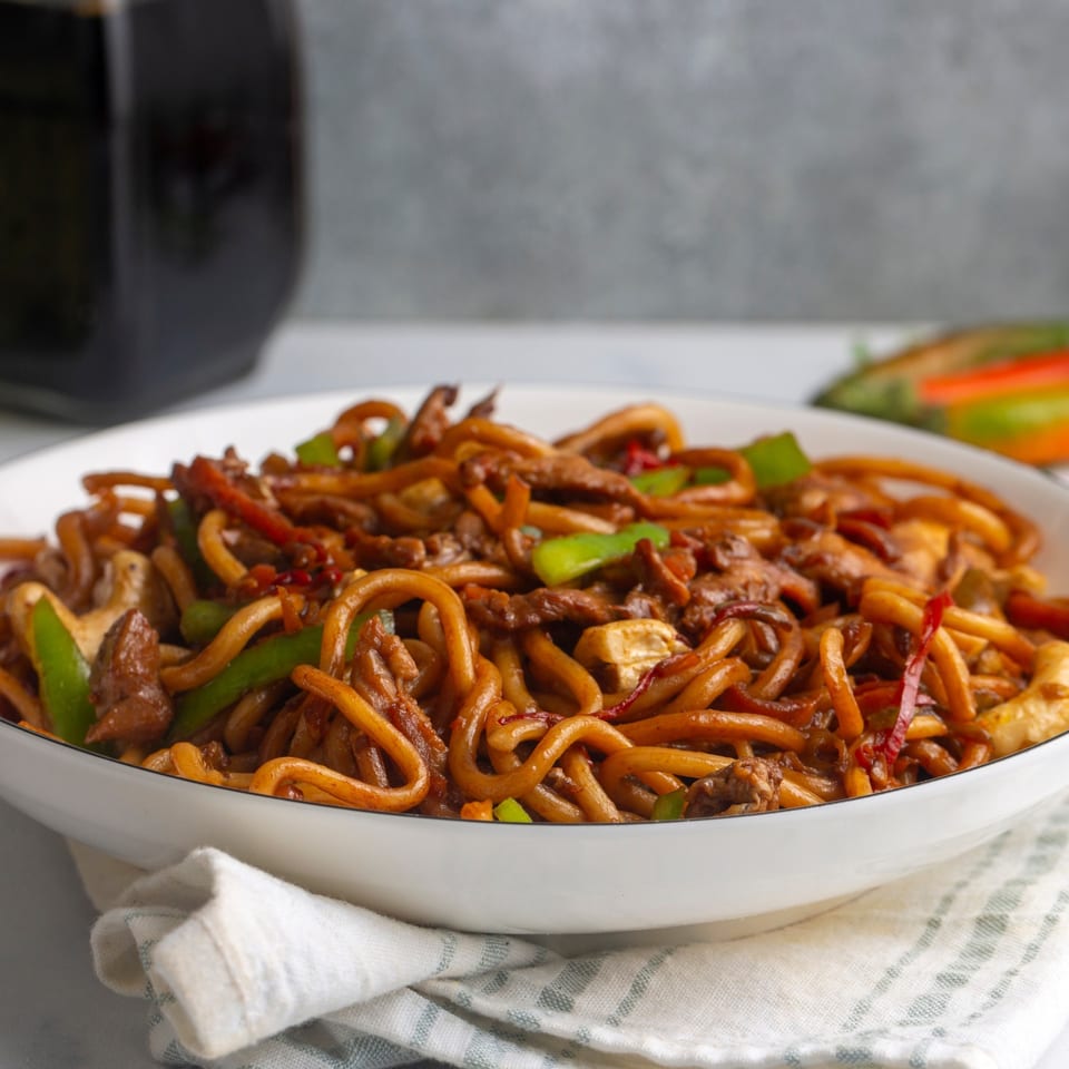 Close-up of a white bowl filled with Himalayan Spice Indian Cuisine's noodles, meat, and vegetables.